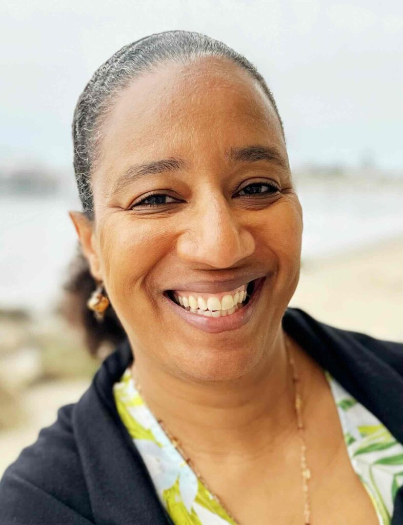 Myriam J.A. Chancy, a Black woman who wears a printed white shirt, black sweater, and hair in a ponytail.