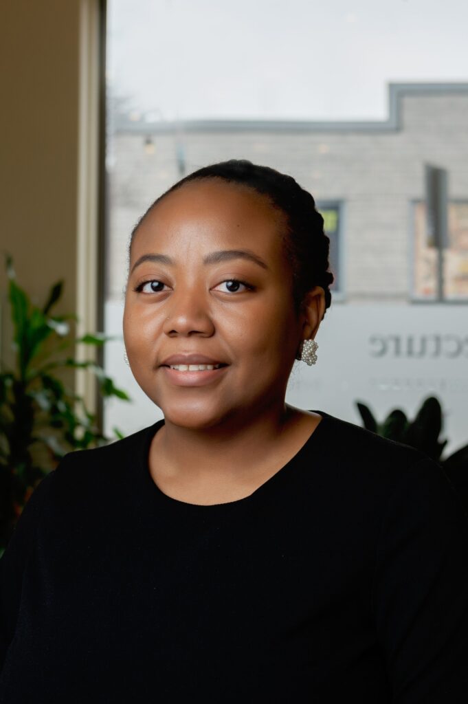 a Black woman with her hair back. She wears a black, dressy top and earrings.