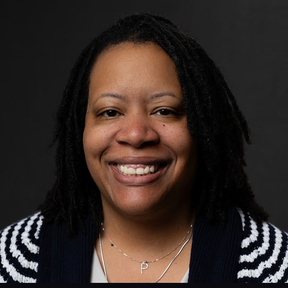 Christian, a middle-aged Black woman, with straight hair past her shoulders. She wears a short-sleeved sweater with black and white stripes.