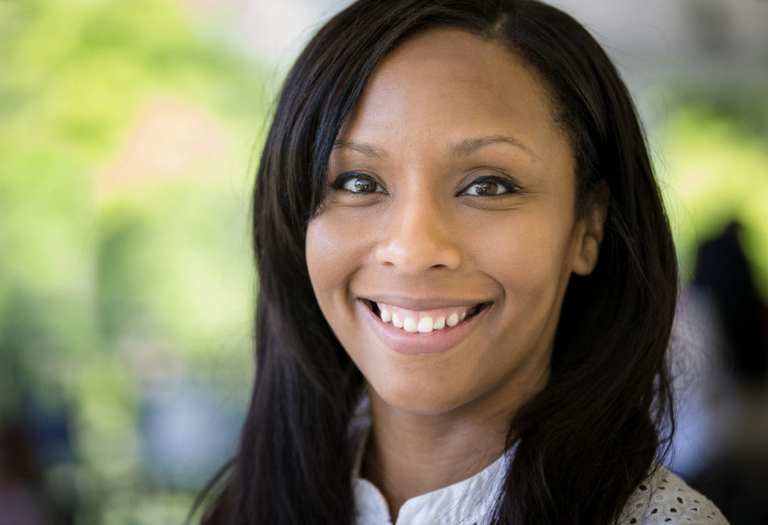 A headshot of Chanel, a young or middle-aged Black woman with black hair a little longer than shoulder-length. In the background, se see an artistically blurry tree.